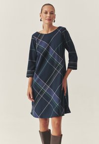 Marineblaues Karokleid mit Dreiviertelärmeln, das ein geometrisches Muster in Grün und Lila aufweist. Hergestellt aus weichem Stoff mit einer lockeren Passform.