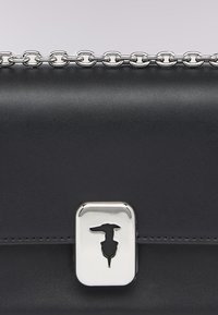 Borsa a tracolla in pelle nera con una catena argentata, dotata di una chiusura metallica con una silhouette di un cane. Tessuto liscio e forma rettangolare.
