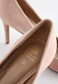 Rosa mockalädershöga klackar med spetsig tå, med en guldig "FOREVER COMFORT"-logotyp på innersulan och en slät inredningsfoder.