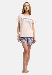 Ljusrosa bomulls-T-shirt med blått tryck som säger "bruno banani NOT FOR EVERYBODY," kombineras med blå shorts som har ett prickigt mönster.