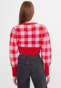 Maglione corto a quadri rossi e rosa con tessuto strutturato e maniche a palloncino, abbinato a jeans scuri a vita alta.