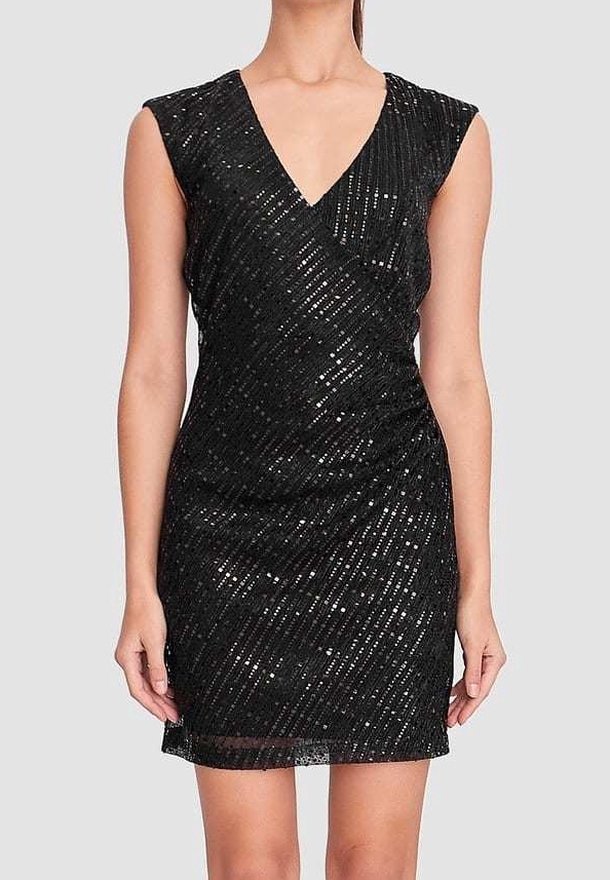 Femme portant une mini-robe noire sans manches à sequins, col en V et motif à rayures diagonales sur fond gris clair.