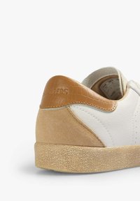 White sneaker with tan suede and crocodile-textured leather accents, featuring a textured rubber sole and perforated sides for breathability.