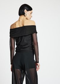 Haut noir à épaules dénudées avec un design drapé et des manches longues transparentes, associé à un pantalon noir transparent, mettant en valeur des textures lisses.