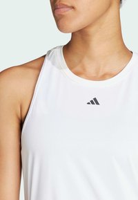 Bijela sportska majica bez rukava s okruglim izrezom. Ima suptilne šavove i mali sivi logo na području grudi.