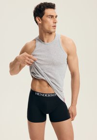 Szary bawełniany tank top, czarne bokserki z gumką "HENDERSON". Model pozuje, podciągając koszulkę, podkreślając materiał i dopasowanie.