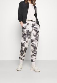 Svart zip-up jacka med strukturerad kropp, kombinerad med vida, mönstrade byxor i vitt och svart. Neutrala sneakers fulländar outfiten.