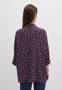 Maroon blouse with a floral pattern in light blue. Features a collar, three-quarter sleeves, and a relaxed fit. Smooth texture.