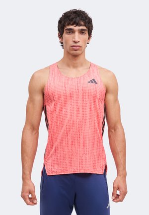 Mann trägt ärmelloses Sporttop mit korallenfarbenem Muster und marineblaue Sportshorts, steht vor hellem Hintergrund.
