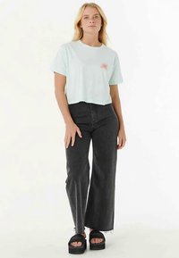 Lichtblauw cropped t-shirt met zonafbeelding, gecombineerd met donkere wijdvallende jeans en zwarte plateauzandalen. Soepele stof, losse pasvorm.