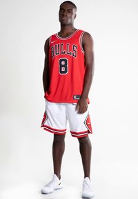Rød basketballtrøje med sort "BULLS" tekst og nummer 8, kombineret med hvide shorts med røde detaljer. Bruges med hvide sportssko.