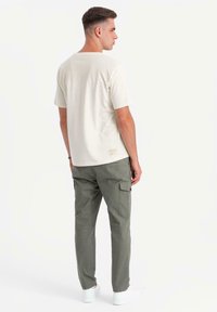 Lysbeige kortærmet t-shirt med en diskret sømdetalje, parret med grønne cargo-bukser med sidelommer, iført hvide sneakers.