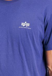 Karameli zila kokvilnas T-kreklu ar apaļu kakla izgriezumu un īsām piedurknēm. Izteiksmīgs balts logo ar abstraktu dizainu uz krūšu daļas.