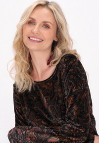 Černý sametový top s vzorovaným potiskem obsahujícími složité paisley vzory v oranžových a burgundských tónech, s kulatým výstřihem a dlouhými rukávy.