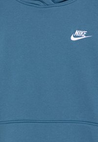 Mėlynas medvilninis džemperis su baltu Nike logotipu krūtinėje ir matomu siuvimo detaliu. Lygi tekstūra su gobtuvu.