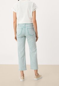 Jeans de mezclilla azul claro con un ajuste relajado y un largo recortado. Presentan dos bolsillos traseros y un detalle de costura en contraste. Llevados con una blusa blanca.