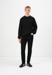 Maglione nero a maglia rasata, pantaloni neri slim-fit, sneakers nere con strisce bianche. Design semplice, maglia texturizzata, schema di colori abbinato.