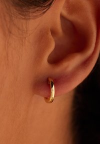 Boucle d'oreille en or présentée dans le lobe de l'oreille, dotée d'une surface lisse et polie avec une forme circulaire, mise en valeur par des teintes de peau.
