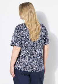 Navy modré tričko s krátkým rukávem a bílým paisley vzorem, navržené v uvolněném střihu. Měkká tkanina s hladkou strukturou a kulatým výstřihem.