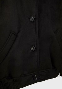 Veste noire avec trois boutons ronds visibles, deux poches latérales inclinées et une ceinture élastiquée au bas de l'ourlet.