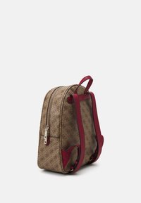 Mochila marrón con un patrón y detalles rojos, que cuenta con dos correas ajustables, cierre de cremallera y un pequeño detalle metálico en la cremallera.