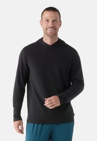 Schwarzer Langarm-Hoodie mit lockerer Passform, aus weichem Stoff, mit doppellagiger Kapuze und nahtlosen Bündchen, getragen mit blauen Shorts.