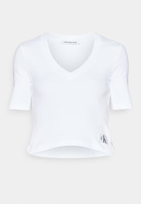 Valkoinen lyhyt toppi, joka on valmistettu ribatusta kankaasta. Siinä on V-pääntie ja lyhyet hihat. Huomattava CK-logo tagi vasemmalla etupuolella.