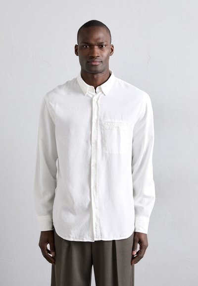 Chemise blanche à manches longues et poche poitrine, en tissu léger, avec une coupe décontractée et un ourlet arrondi.