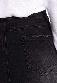 Czarne dżinsy o wysokim stanie, z tylną kieszenią i subtelnymi przeszyciami. Gładka faktura i dopasowany krój.