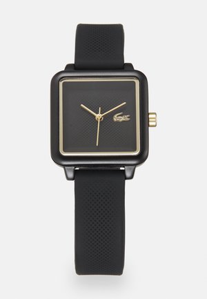 Montre carrée noire avec un cadran texturé, accents dorés sur les aiguilles et le boîtier, et un bracelet en silicone noir mat arborant un logo de crocodile.