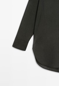 Dunkelgraues Langarmshirt mit abgerundetem Saum, aus einem strukturierten Stoff gefertigt. Verfügt über einen geknöpften Ärmel und eine lockere, entspannte Passform.