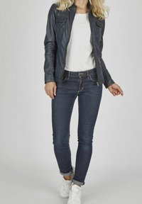 Tmavě modrá kožená bunda na zip se dvěma náprsními kapsami, doplněná tmavě modrými džínami a bílými teniskami, vytvářející ležérní outfit.