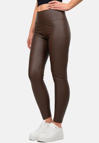 Leggings marroni a vita alta realizzati in un materiale lucido ed elastico, con una superficie liscia e senza motivi o loghi visibili, abbinati a scarpe da ginnastica bianche.