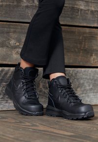 Black leather and mesh ankle boots with round toe, padded collar, and sturdy laces. Textured finish with rubber outsole, set against wooden background.