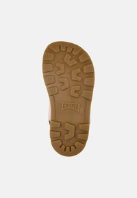 Ruskea kumipohja, jossa on teksturoidun kuvion, jossa on painettuna "CAMPER" -logo ja koko "28". Yläsivut vaaleanpunaisina ja oliivinvihreinä.