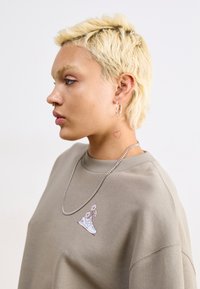 Hanorac gri cu un grafic de sneakers florali, având decolteu rotund și umeri lăsați. Cerceii cu lanț argintiu, cercei cerc și tatuaj vizibil.