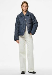 Tamsiai mėlynas quilted švarkas su dideliu apykakle, mygtukų uždarymu ir kišenėmis. Dėvimas su baltais plačiais kelnais ir juodais batais.