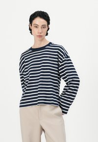 Top de rayas en azul marino y blanco de manga larga con cuello redondo y corte relajado. Presenta un pequeño logotipo de la marca en el pecho.
