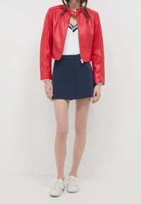 Rode cropped jas van nepleer met drukknoopkraag, marineblauwe minirok en witte sneakers. De outfit heeft een sportief casual ontwerp.