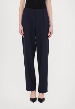Pantalons tailleur navy avec plis, confectionnés à partir d'un tissu lisse. Dotés d'une fermeture à un bouton et de jambes droites, accompagnés de talons noirs.