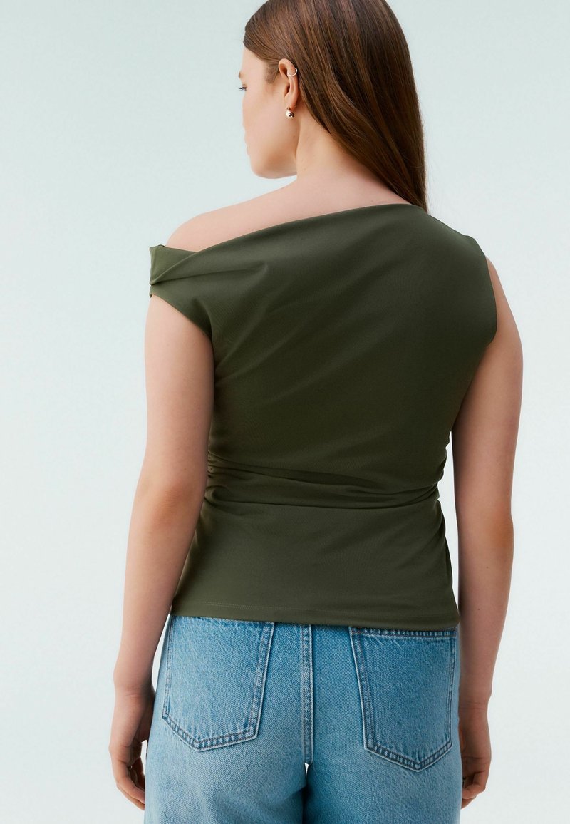 Top olive vert décolleté avec des manches courtes et un détail froncé sur le côté, associé à un jean en denim léger taille haute bleu clair.