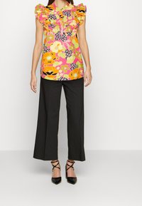 Floral top featuring multicolored patterns and ruffled sleeves, paired with black wide-leg trousers and pointed black heels.