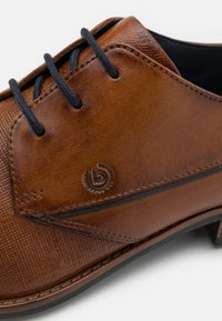 Scarpa in pelle marrone con finitura testurizzata, lacci neri, cuciture a contrasto, dettaglio del logo e suola piatta.