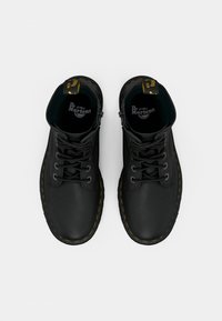 Black leather boots with a textured finish, round toe, yellow stitching, lace-up front, and branded tongue, featuring an interior logo.