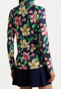Camisa de manga larga en color marino con un vibrante estampado floral en rojo, amarillo y verde. Presenta un cuello alto y un ajuste ceñido, con un detalle de cremallera en la parte posterior.