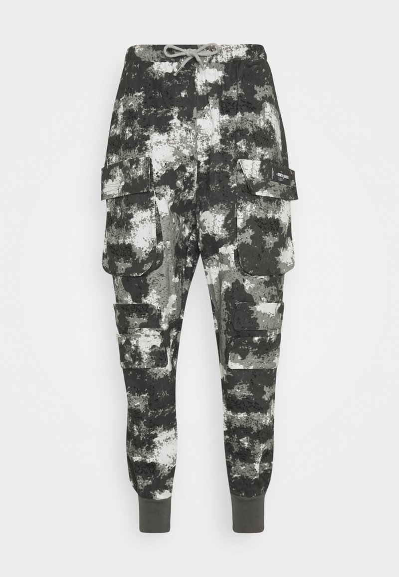 Pantalones cargo en un patrón de camuflaje negro, gris y blanco. Con múltiples bolsillos laterales y puños elásticos en los tobillos. Tela suave.