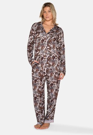 Vrouw staat op blote voeten en draagt een bijpassende paisley-gebloemde pyjamablouse en broek met zakken tegen een witte achtergrond.