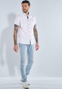 Kurze Ärmel, hellrosa gestreiftes Hemd mit Knopfleiste. Getragen mit hellblauen Jeans und weißen Sneakers, die schwarze Knöpfe und umgeschlagene Ärmel haben.