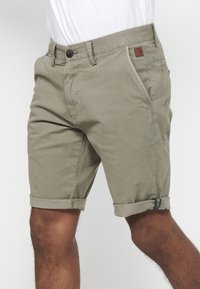 Lichtbeige textuurshorts voor heren met opgerolde manchetten, voorkruiszakken, knoopsluiting en een klein bruin logopatch op de tailleband.