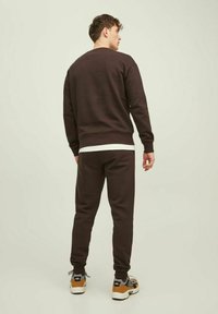 Bruine sweatshirt en bijpassende joggingbroek van zachte stof. Bevat een ronde halslijn en elastische boorden, gecombineerd met een witte onderhemd en sneakers.